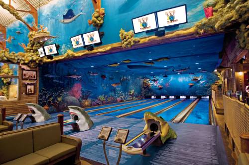 A vibrant bowling alley with an underwater theme, featuring colorful murals of sea life and shark-shaped bowling lanes.