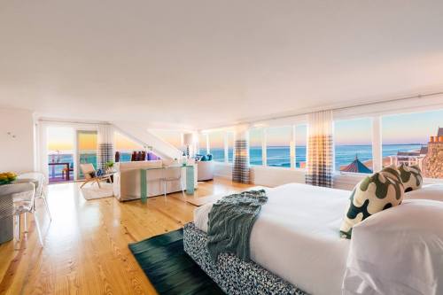 Bright, modern bedroom with ocean views, large windows, and stylish decor, featuring two beds and a cozy seating area.