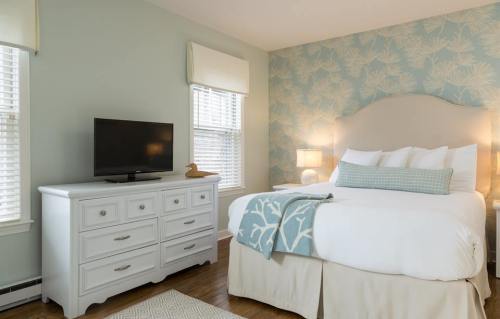 Cozy bedroom with a light blue wall, a white bed, dresser, TV, and decorative accents.