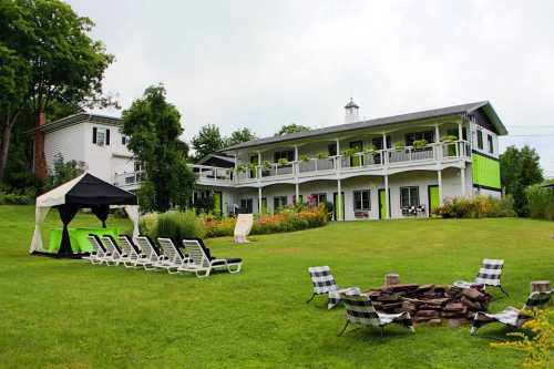 A green and white building with a balcony, surrounded by a lawn, lounge chairs, and a fire pit.