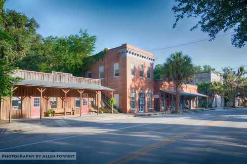 Historic buildings line a quiet street, surrounded by lush greenery and palm trees under a clear blue sky.