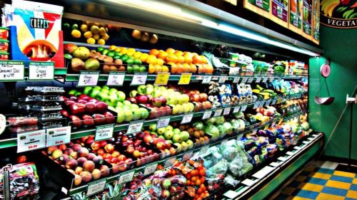 A colorful display of various fruits and vegetables in a grocery store, neatly arranged on shelves.