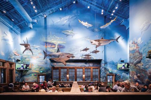 A vibrant restaurant interior with ocean-themed murals and fish sculptures, filled with diners enjoying their meals.