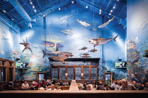 A vibrant restaurant interior with ocean-themed murals and large fish sculptures, filled with diners enjoying their meals.