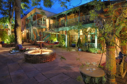 A cozy courtyard with colorful buildings, lush greenery, and a fire pit, illuminated in the evening glow.