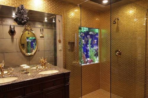 Luxurious bathroom with gold mosaic tiles, dual sinks, a large mirror, and a glass-enclosed fish tank.