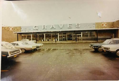 A vintage photo of a store named "GRAVES" with parked cars in front and a cloudy sky.