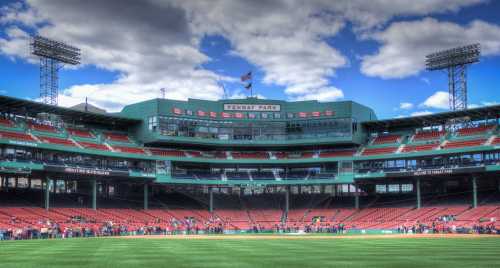 A wide view of Fenway Park, showcasing empty red seats and a cloudy sky above the iconic stadium.