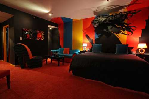 A vibrant hotel room with bold colored walls, a large bed, colorful furniture, and artistic decor.