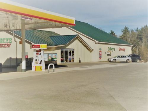 A gas station and grocery store with a green roof, parked cars, and a clear sky in the background.
