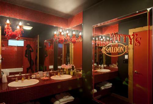 A stylish bathroom with red tile, dual sinks, and a mirror featuring "Kitty's Saloon" in bold lettering.