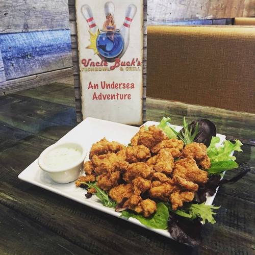 A plate of crispy fried food on a bed of greens, accompanied by a small cup of dipping sauce, next to a sign for Uncle Buck's.