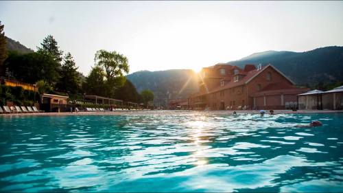 A serene pool scene at sunset, surrounded by mountains and a building, with people swimming in the water.