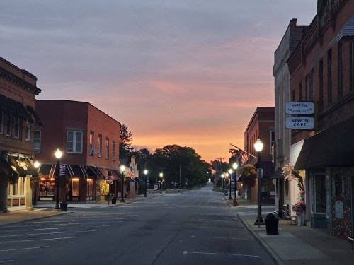Quiet downtown street at sunrise, with shops lining the road and a colorful sky in the background.