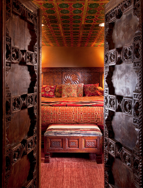 A beautifully decorated room with intricate wooden doors, colorful textiles, and a patterned ceiling.