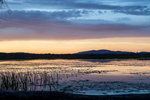 A serene lake at sunset, with colorful clouds reflecting on the water and mountains in the background.