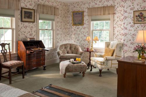 Cozy room with floral wallpaper, a vintage writing desk, armchairs, and soft lighting, creating a warm atmosphere.