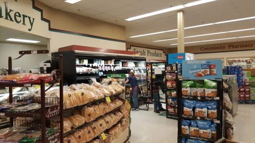 A grocery store interior featuring a bakery section, fresh produce, and shelves stocked with snacks and organic items.