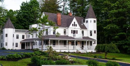 A large white Victorian-style house with turrets, surrounded by greenery and a well-maintained garden.