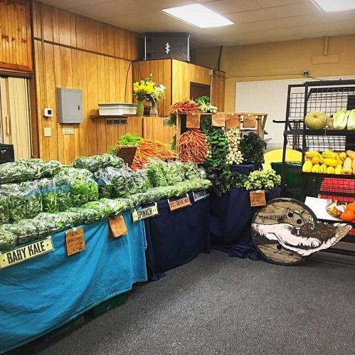 A market display featuring various fresh vegetables, including greens, carrots, and squash, in a wooden room.