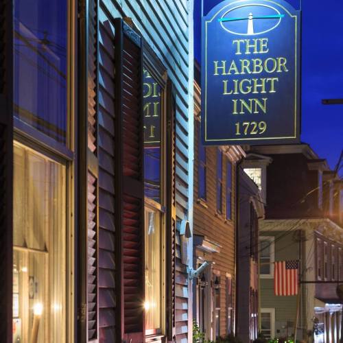 A historic inn sign illuminated at night, surrounded by charming buildings and a flag in the background.