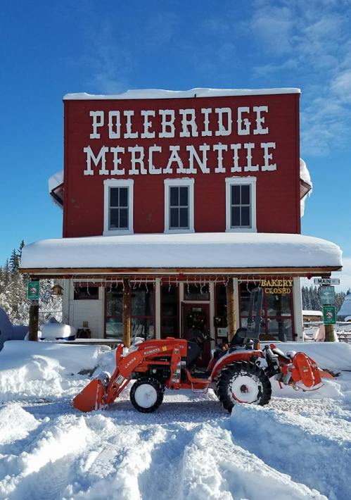 A red mercantile building with "Polebridge Mercantile" sign, snow-covered ground, and a tractor in front.