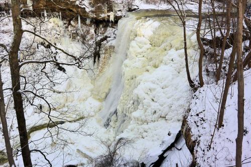 A frozen waterfall surrounded by snow-covered trees and rocky cliffs, creating a serene winter landscape.