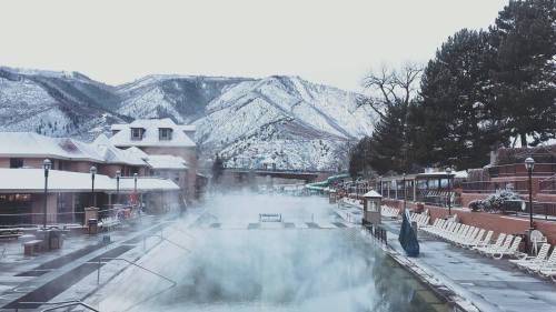 A snowy landscape featuring a steaming hot spring pool surrounded by mountains and a resort.