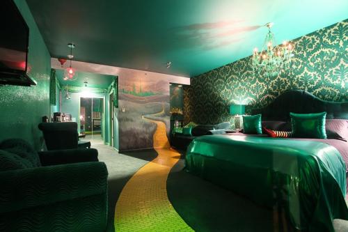 A stylish hotel room with green lighting, a large bed, decorative wallpaper, and a unique mural on the wall.