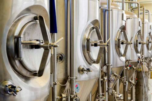 Close-up of stainless steel fermentation tanks in a brewery, showcasing valves and industrial design.