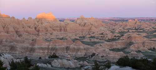 A panoramic view of rugged, colorful rock formations at sunset in a vast, open landscape.