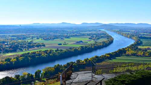 A scenic view of a winding river surrounded by lush green fields and distant mountains under a clear blue sky.