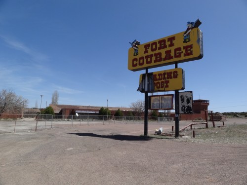 Sign for Fort Courage, an abandoned building with a fenced area and clear blue sky in the background.