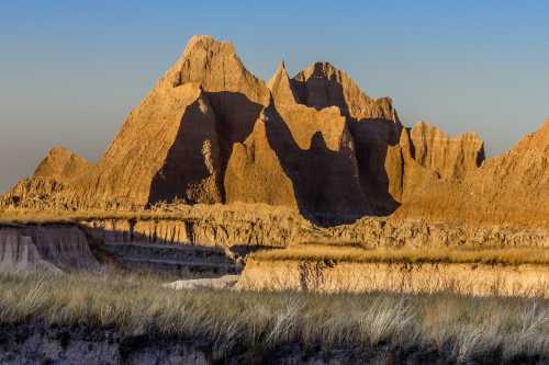 A rugged mountain landscape with sharp peaks and grassy plains under a clear blue sky.