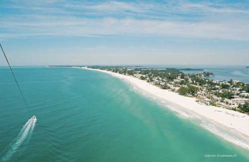 Aerial view of a serene beach with turquoise waters, white sand, and a boat cruising along the coastline.