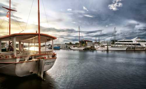 A serene marina scene featuring a wooden boat and various yachts under a cloudy sky at sunset.