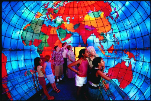A group of people exploring a colorful, illuminated globe map in an interactive exhibit.