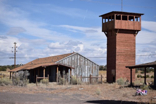 Abandoned building and watchtower in a desolate landscape under a blue sky with scattered clouds.