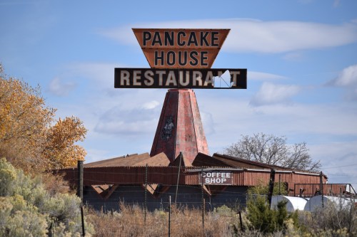 A vintage Pancake House restaurant sign stands tall against a blue sky, surrounded by trees and shrubs.