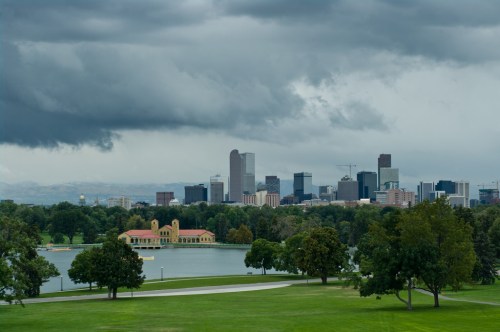 A cloudy skyline of Denver, Colorado, with a lake and green park in the foreground.