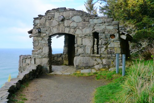 Stone structure with an archway overlooking the ocean, surrounded by greenery and trees.