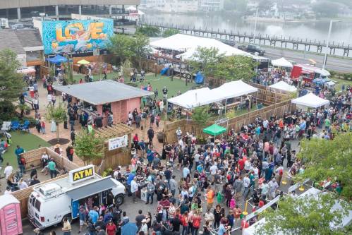 A bustling outdoor market scene with food trucks, tents, and a large crowd enjoying the festivities by the water.