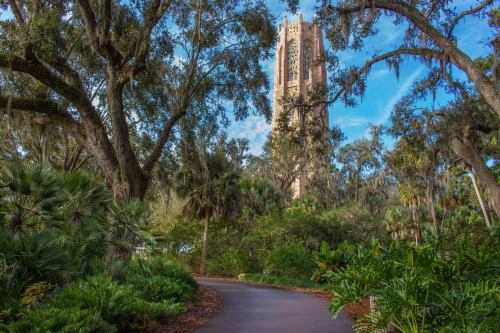 A winding path leads through lush greenery to a tall, ornate tower surrounded by trees and blue skies.