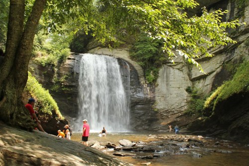 A scenic waterfall surrounded by lush greenery, with people enjoying the water and relaxing on the rocks.