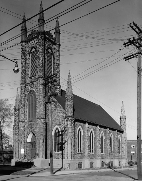 Historic stone church with tall spires, surrounded by power lines and trees, captured in black and white.