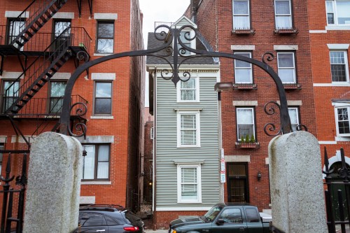 A wrought iron archway frames a narrow building between red brick structures in an urban setting.