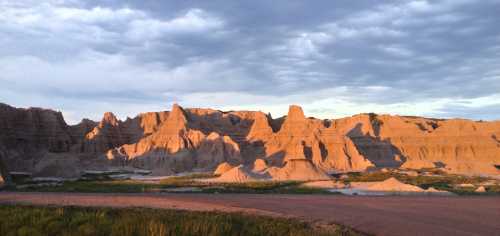 A panoramic view of rugged, layered rock formations under a cloudy sky, with soft sunlight illuminating the landscape.