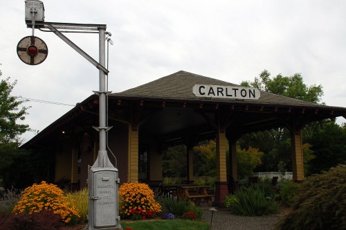 Historic train station in Carlton, featuring a signal post and vibrant flower beds. Overcast sky in the background.