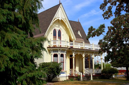 A charming Victorian-style house with intricate details, surrounded by greenery and a clear blue sky.