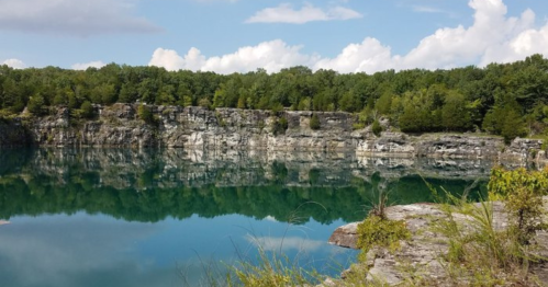 A serene lake surrounded by rocky cliffs and lush green trees under a partly cloudy sky.